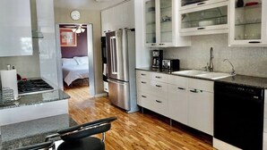 Eine kompakte Küche mit Kühlschrank, Herd und Geschirrspüler. Ein Bett ist im angrenzenden Zimmer zu sehen.