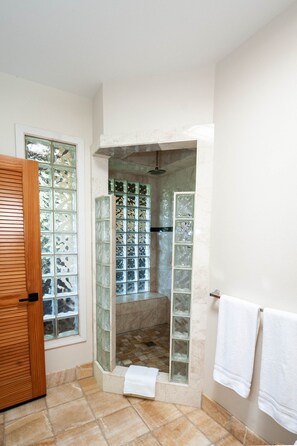 Un baño con cabina de ducha de vidrio, puerta de madera y suelo de baldosas.