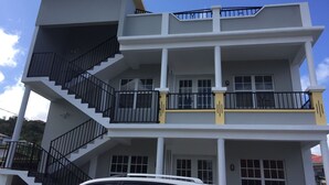 Un immeuble à plusieurs étages doté d’un escalier central, de balcons et d’une voiture garée devant.