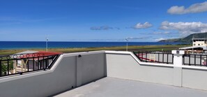 A coastal view with a clear sky, a wind turbine, and a building with a red roof.