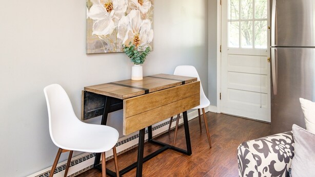 A dining area with a wooden table, two white chairs, a vase with flowers, and a large floral painting on the wall. - Nona's Cottage-Waynesboro/Shenandoah Valley, VA (Waynesboro)