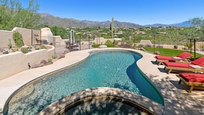 A swimming pool with a curved design, surrounded by a fence and red lounge chairs. - Upscale Home: Amazing Views! Pool & Hot Tub (Tucson)