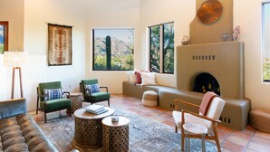 A spacious living room with a fireplace, comfortable seating, and large windows offering mountain views. - Upscale Home: Amazing Views! Pool & Hot Tub (Tucson)