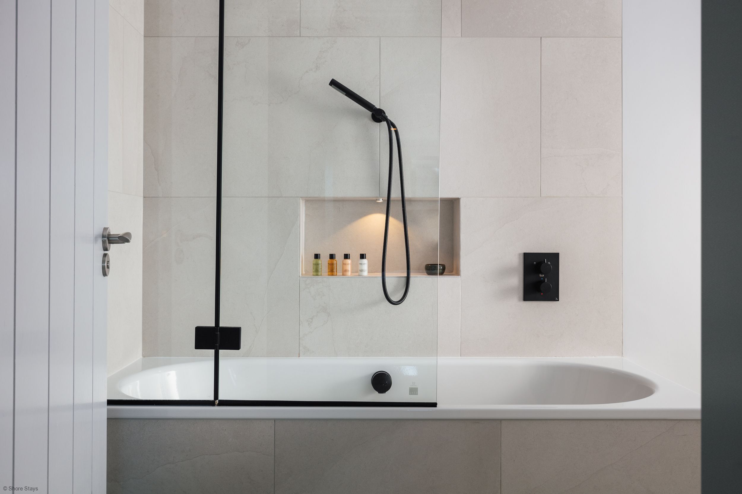 Une salle de bain moderne avec une baignoire sur pieds, une douchette et une étagère contenant des articles de toilette.