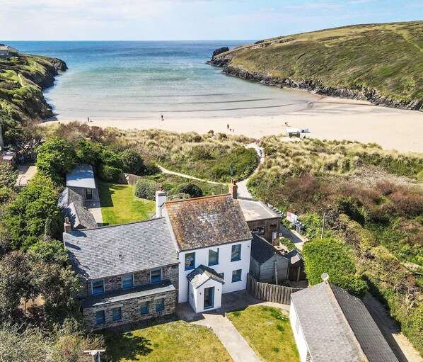 A coastal property with a beach view, stone and white buildings, and a grassy area.