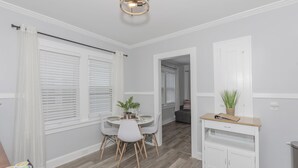 Un coin repas avec une table ronde, des chaises et une petite plante. On y trouve également une console blanche ornée d’une plante et d’un panier.