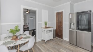 Une cuisine moderne avec un réfrigérateur en acier inoxydable, une table à manger pour quatre personnes et un petit chariot sur lequel est posée une plante.