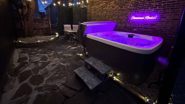 Un espace extérieur aménagé avec un jacuzzi, un sol en pierre, un mur en briques et des guirlandes lumineuses.