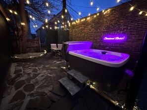 Un espace extérieur aménagé avec un jacuzzi, un sol en pierre, un mur en briques et des guirlandes lumineuses.