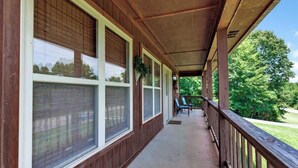Une véranda couverte avec de grandes fenêtres, une balustrade en bois et une vue sur un paysage verdoyant.