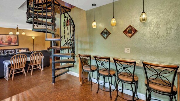 Un espace repas agrémenté d’un escalier en colimaçon, de chaises en bois et de luminaires suspendus.