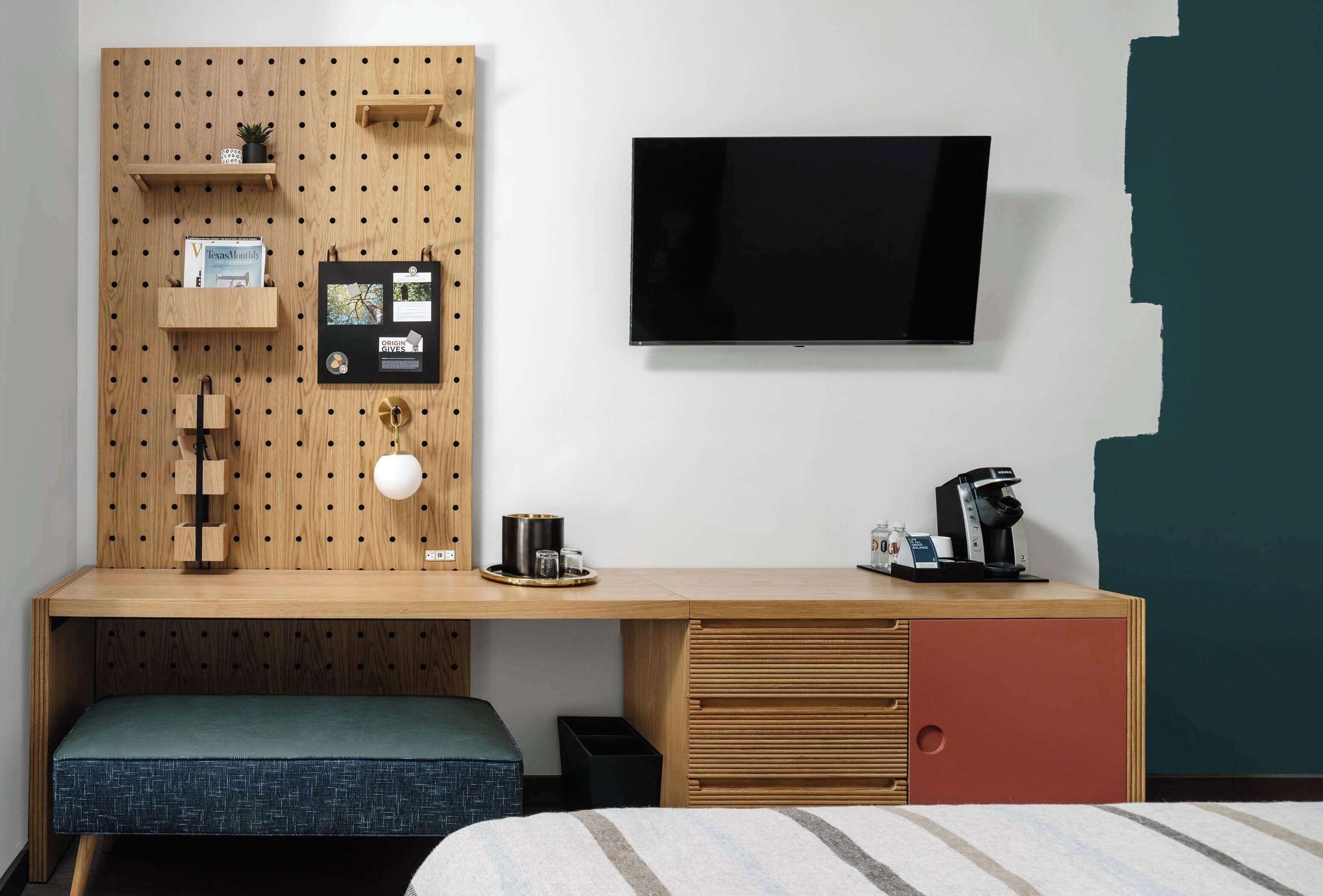A modern room with a wooden desk, a mounted TV, a bench, and a coffee machine.