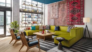 Een moderne woonkamer met een groene bank, houten stoelen, een salontafel en een boekenkast.