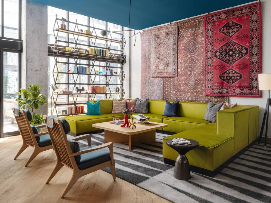 Een moderne woonkamer met een groene bank, houten stoelen, een salontafel en een boekenkast.