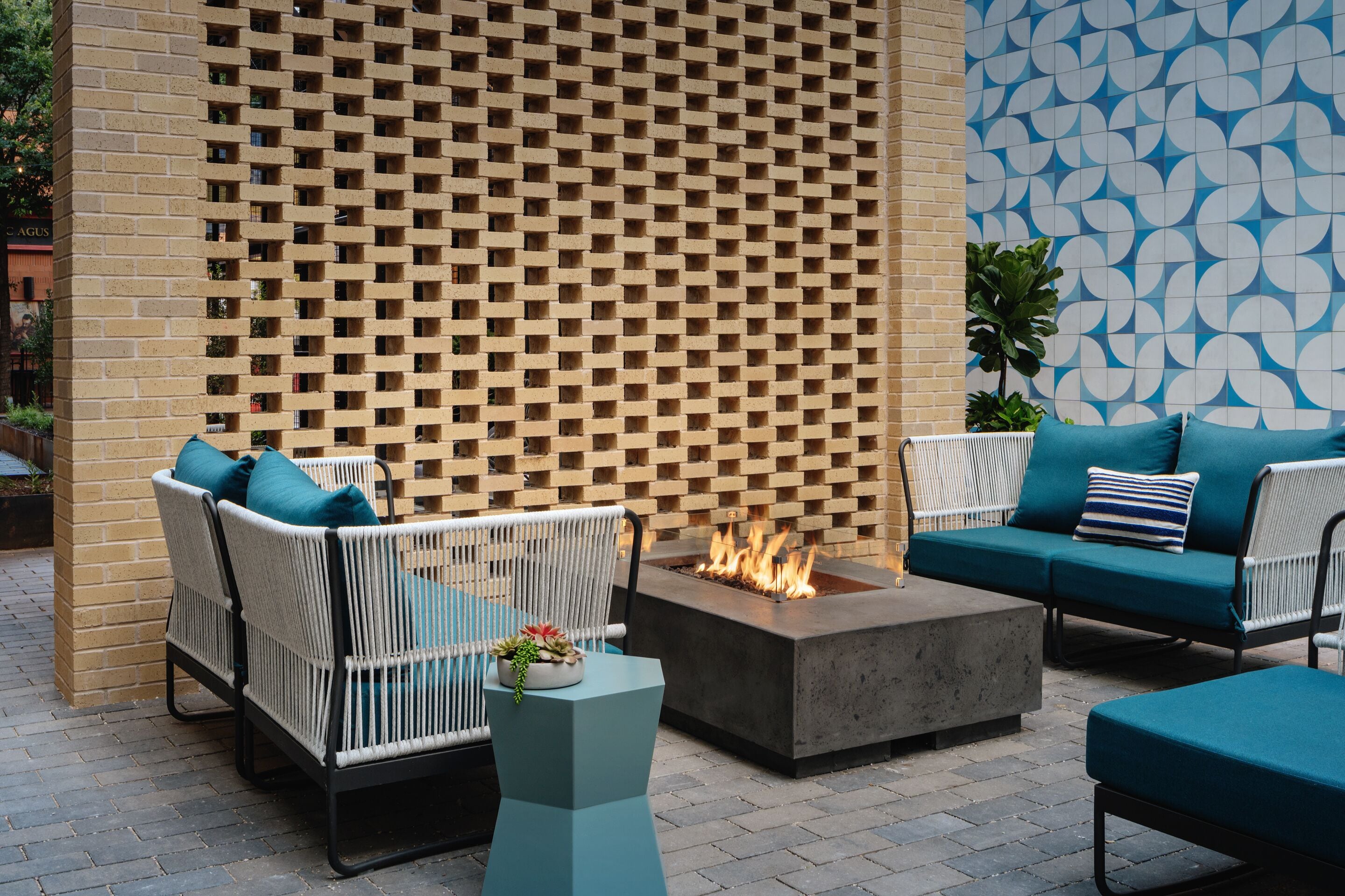 An outdoor seating area with wicker chairs and a sofa, a fire pit, and a patterned wall.