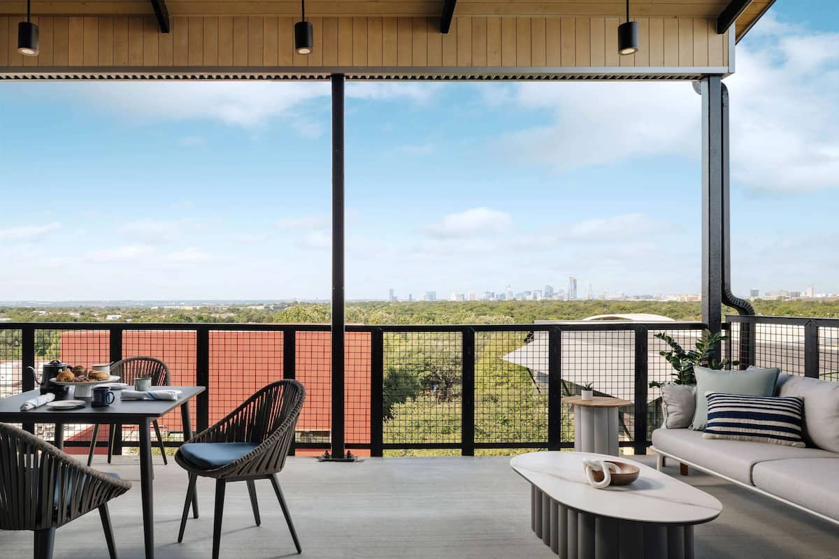 Ein Balkon mit Tisch, Stühlen und einer Sitzecke, mit Blick auf Stadt und Grünflächen.