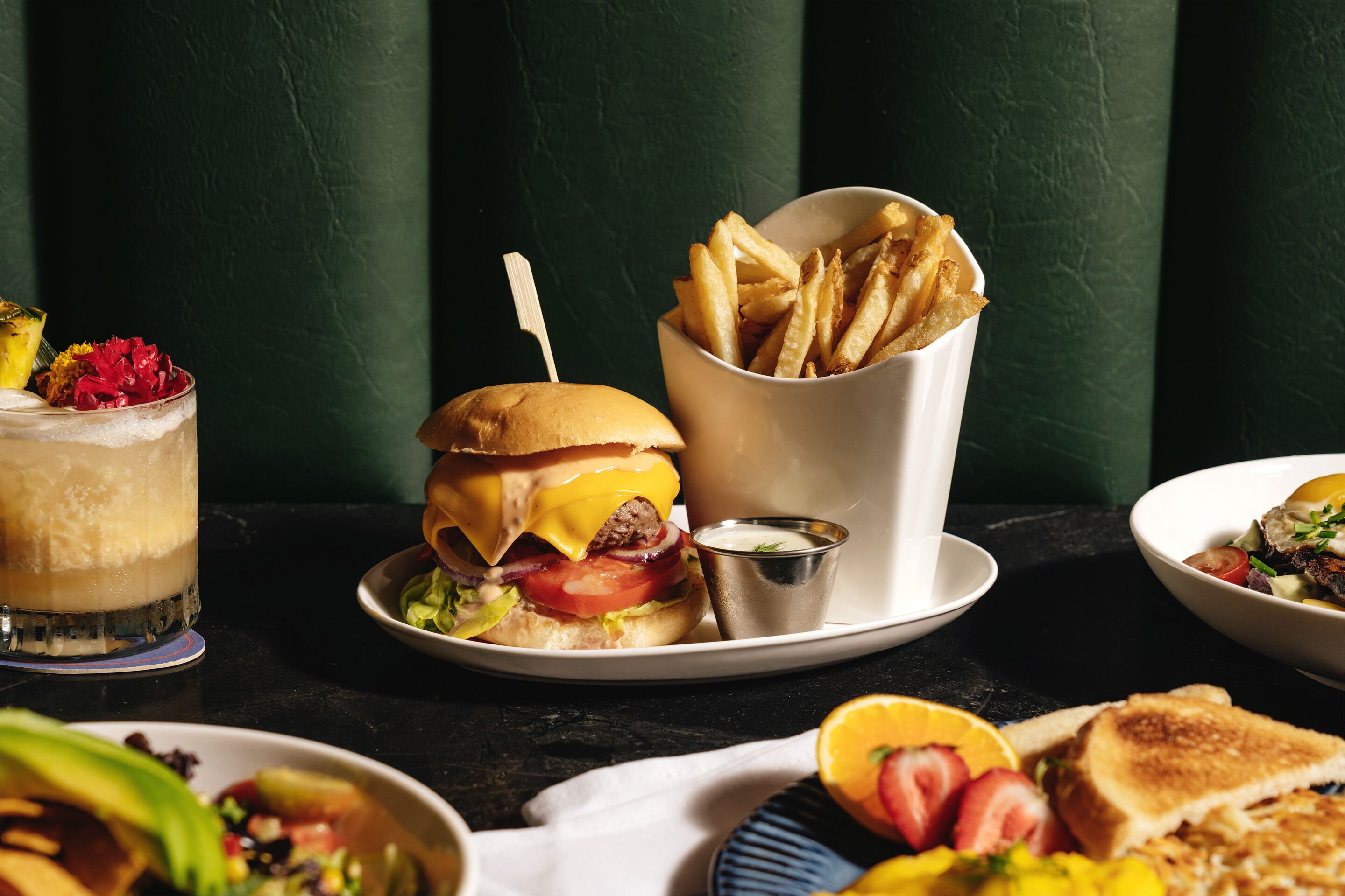 Una comida con una hamburguesa, papas fritas y una bebida sobre una mesa.