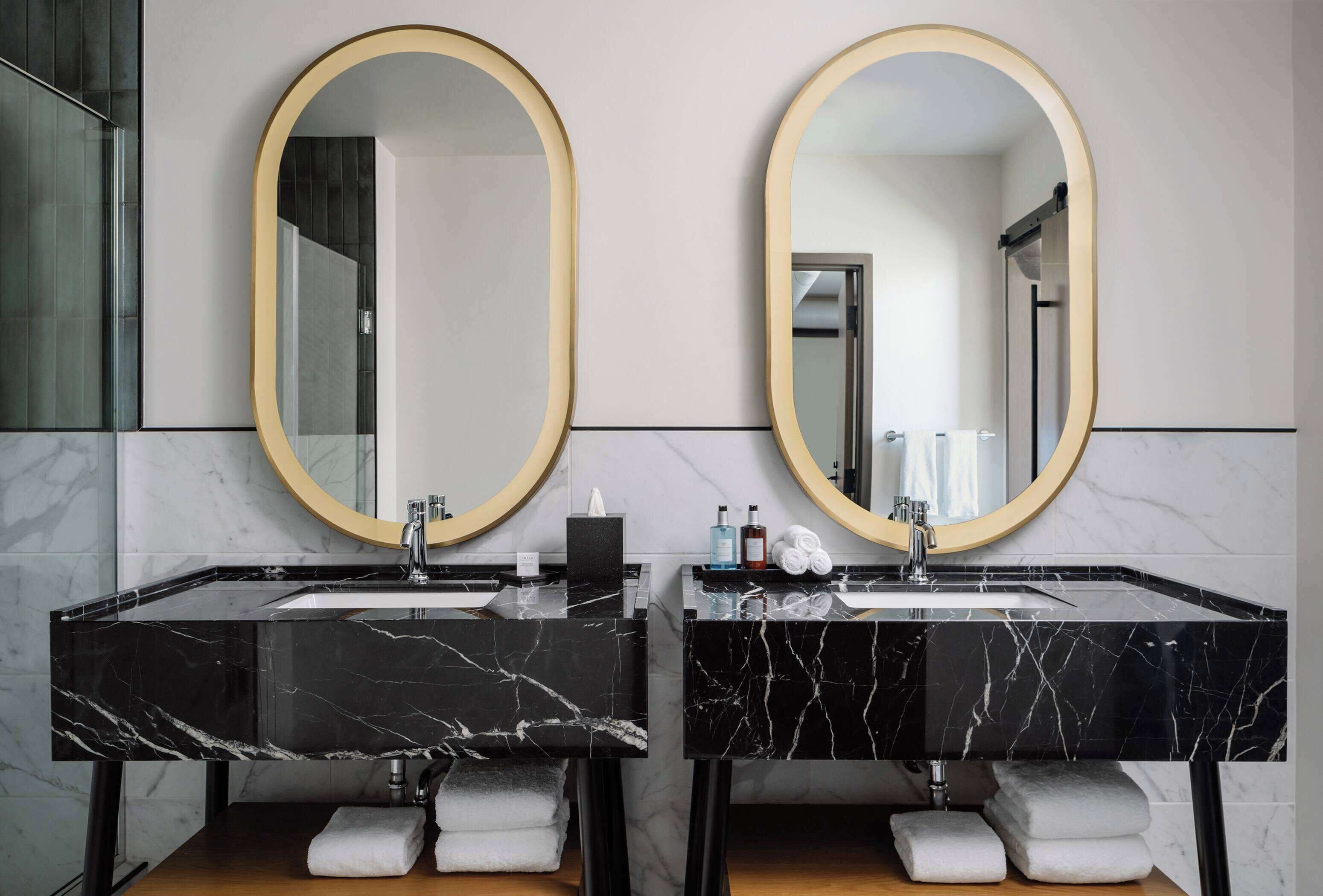 Een moderne badkamer met twee marmeren wastafels, grote spiegels en keurig opgevouwen handdoeken.