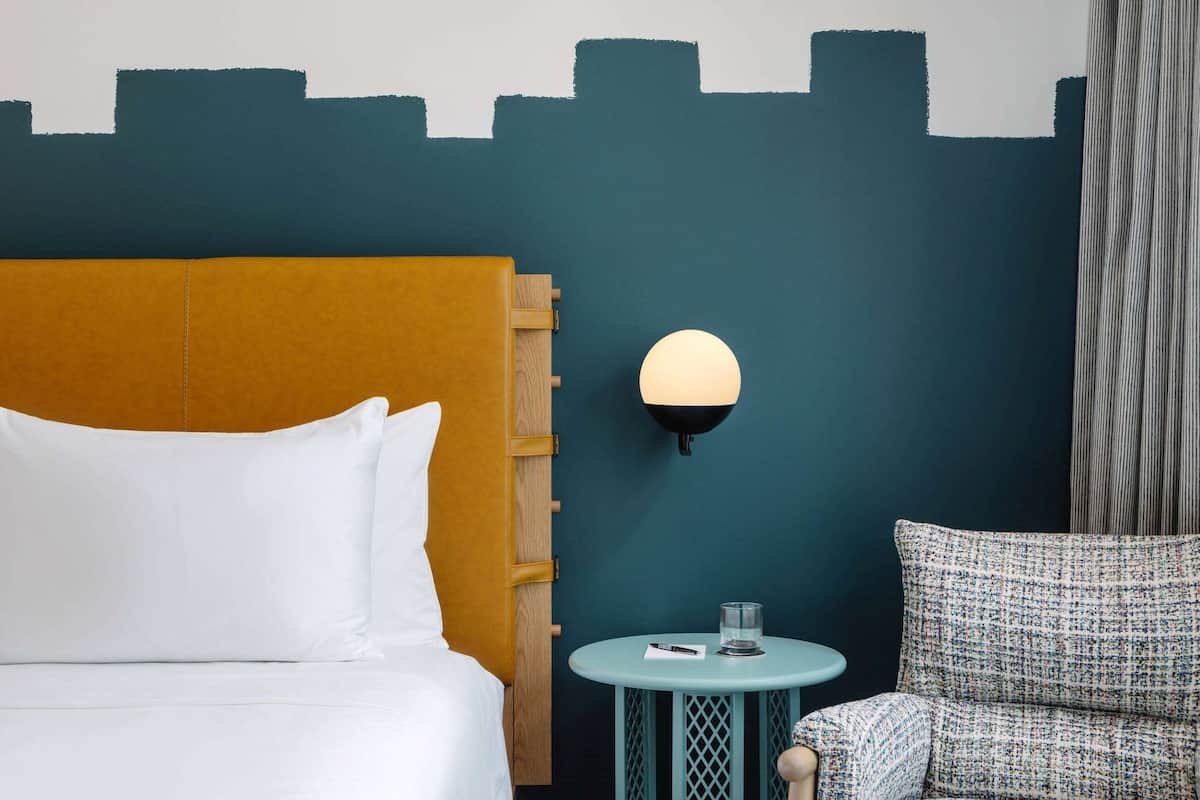 Ein Hotelzimmer mit einem Bett, einem runden Tisch mit Lampe und einer Wand mit Stadtbild-Mural.