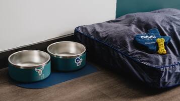Deux gamelles pour animaux de compagnie en acier inoxydable, ornées d’un logo représentant une tête de taureau, un tapis bleu et un panier pour animaux de compagnie avec un jouet.