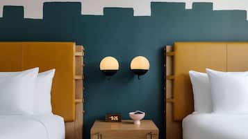 Habitación de hotel con dos camas, una mesita de noche con un reloj y un cuenco, y lámparas fijadas a la pared.