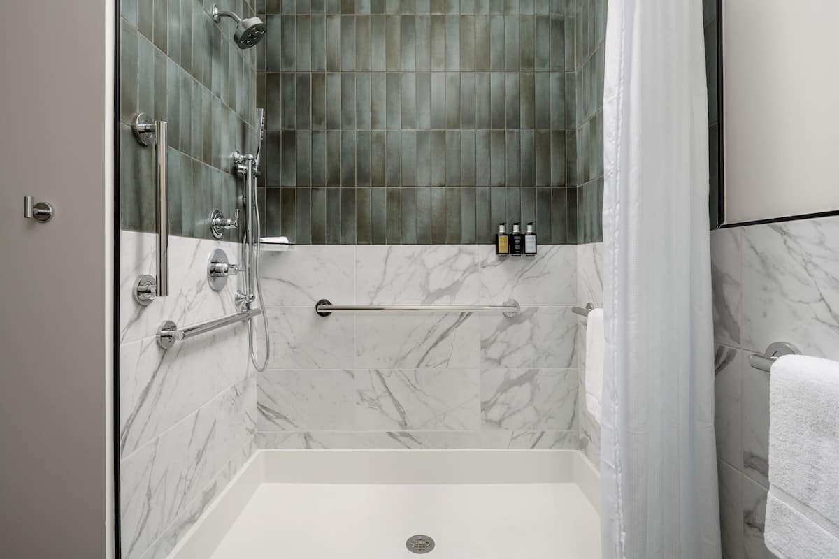 Ein modernes Duschbad mit Glasabtrennung, einer Wand aus Marmorplatten und einer weißen Badewanne.