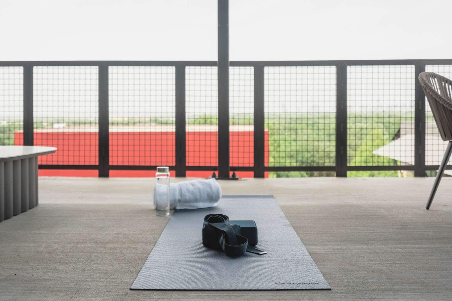 A yoga mat on a balcony with a view of a red building and a green field.