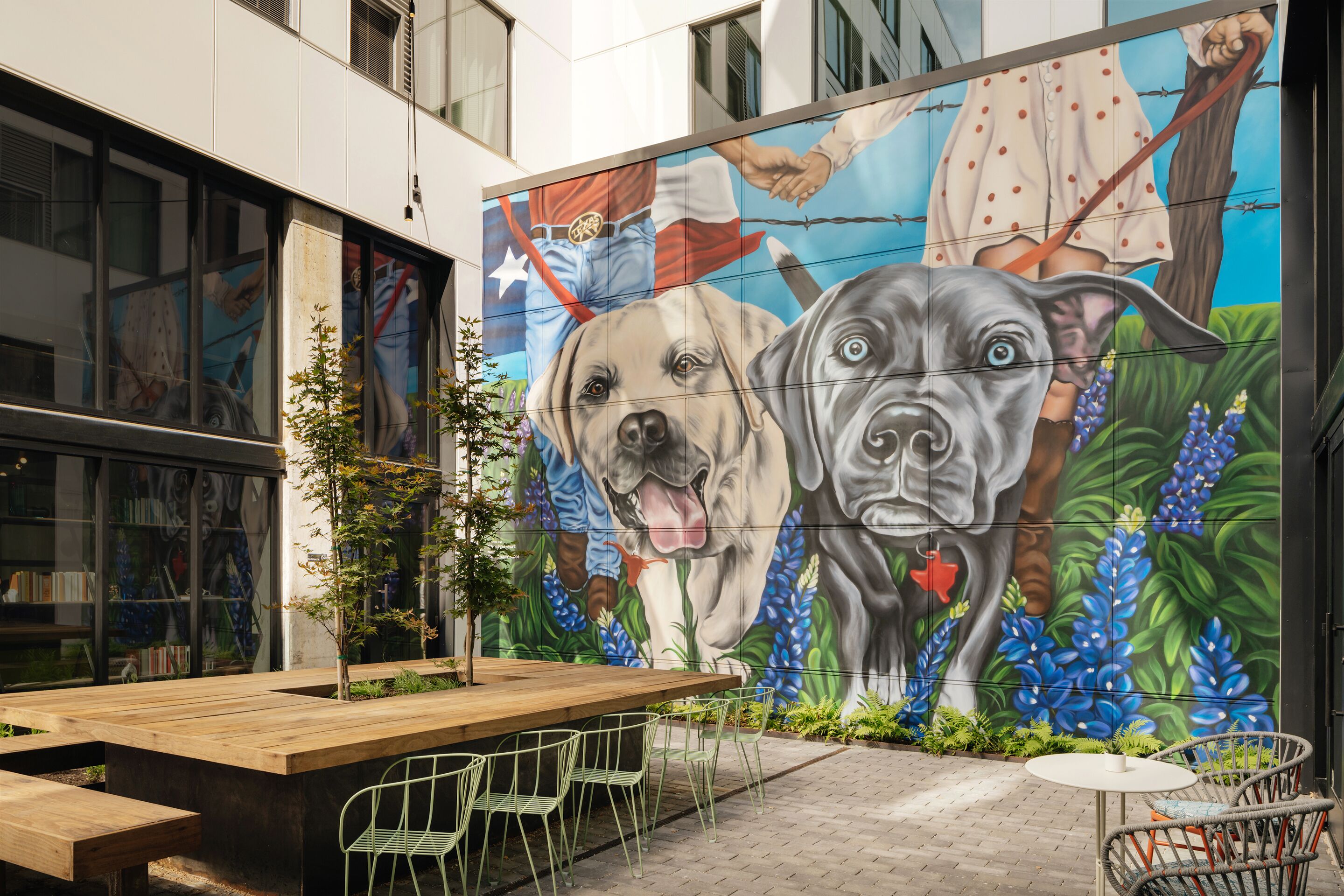 An outdoor seating area with a mural of dogs, a wooden table, and chairs.