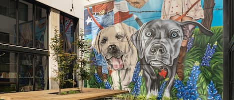 An outdoor seating area with a mural of dogs, a wooden table, and chairs.