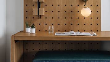 Een houten bureau met een bankje, een kapstok aan de muur, een hanglamp en een kleine plant.