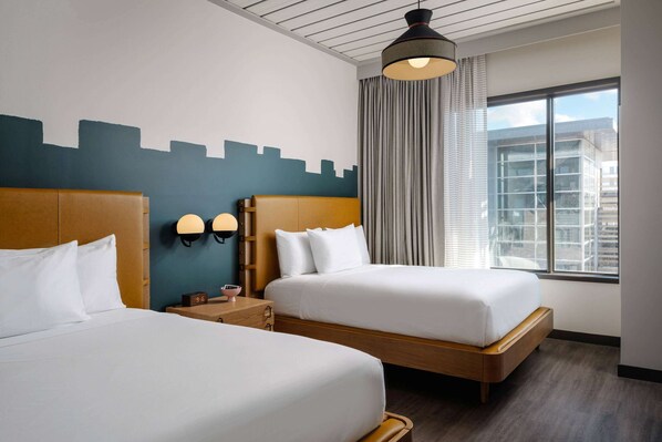 A hotel room with two beds, a cityscape mural, a large window with curtains, and a modern ceiling design.