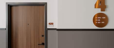Habitación de hotel con puerta de madera, un número '4' fijado a la pared y un cartel circular con números de habitación e indicaciones.
