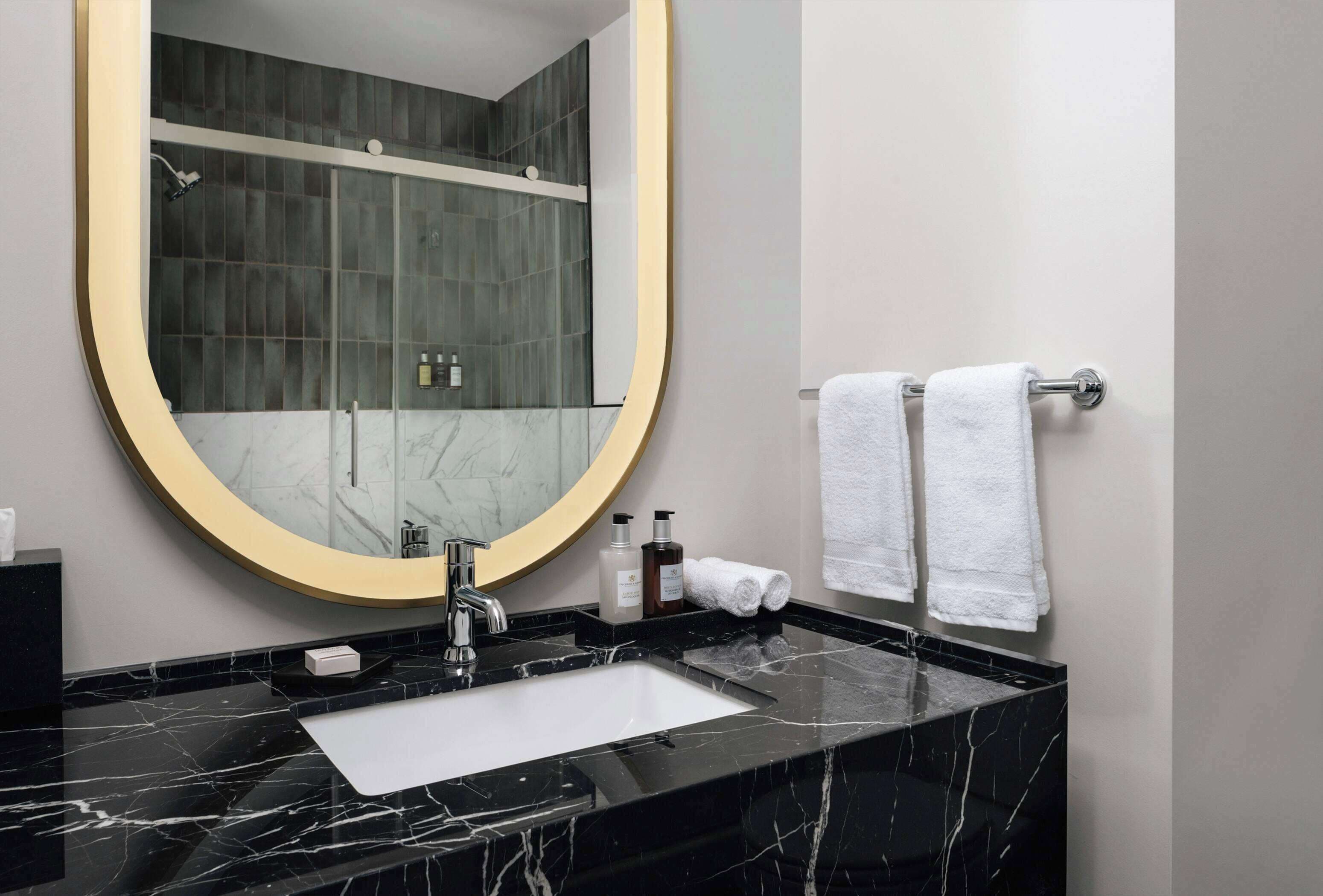 A bathroom with a black marble sink, a large mirror, and a towel rack with two white towels.
