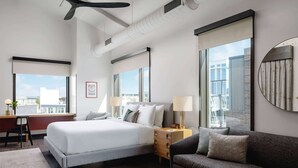 Ein modernes Hotelzimmer mit einem großen Bett, einer Couch, einem Schreibtisch und Blick auf die Stadt.
