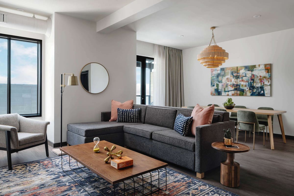 Ein modernes Wohnzimmer mit einem Ecksofa, einem Couchtisch, einem Essbereich und einem großen Fenster mit Blick.
