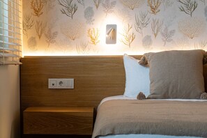 A bedroom with a wooden headboard, a bedside table, a bed with a beige blanket, and a wall with a marine life wallpaper.