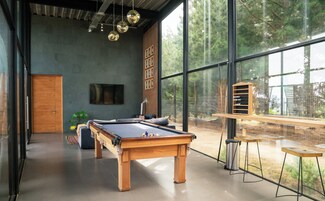 Una mesa de billar moderna en interior, con un ventanal y vistas a árboles.