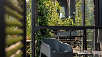 Una terraza moderna al aire libre con una silla y una mesa minimalistas, rodeada de exuberante vegetación y una pérgola de madera.