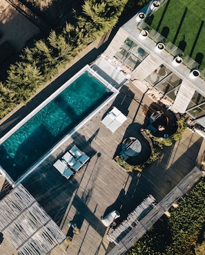 An aerial view of a rooftop pool area with clear water, surrounded by wooden decking, lounge chairs, and a circular seating area with a central fountain. - Taka Matanzas (Navidad)