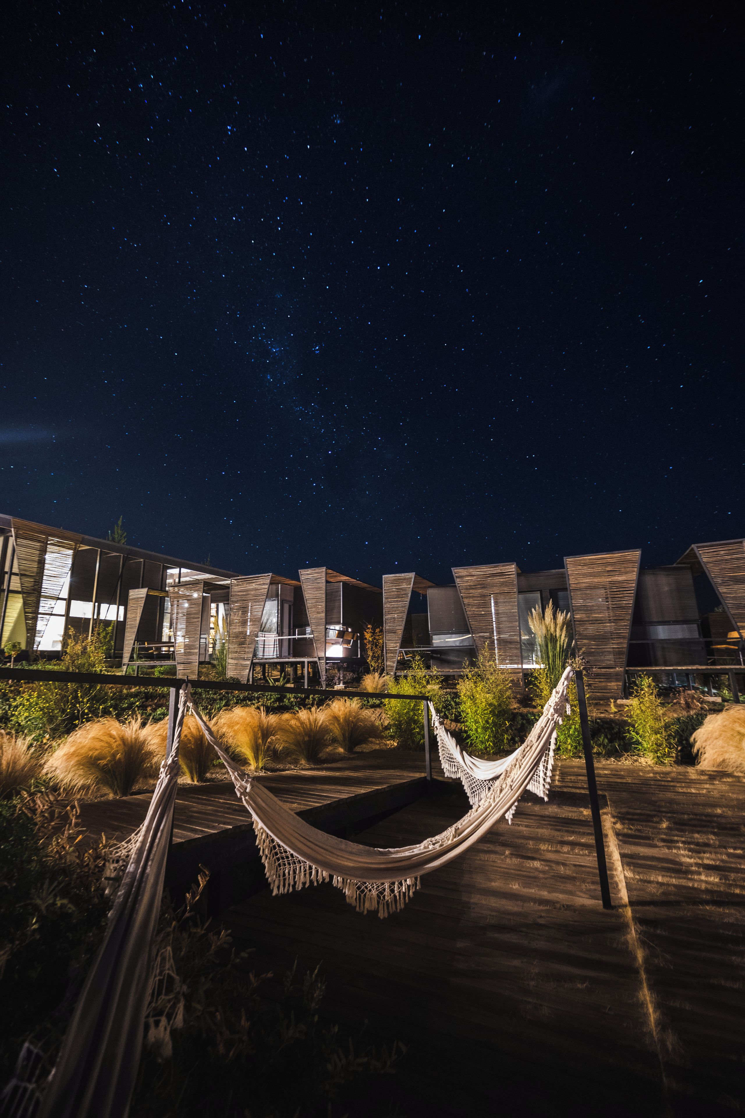 A starry night sky with a hammock and modern buildings.