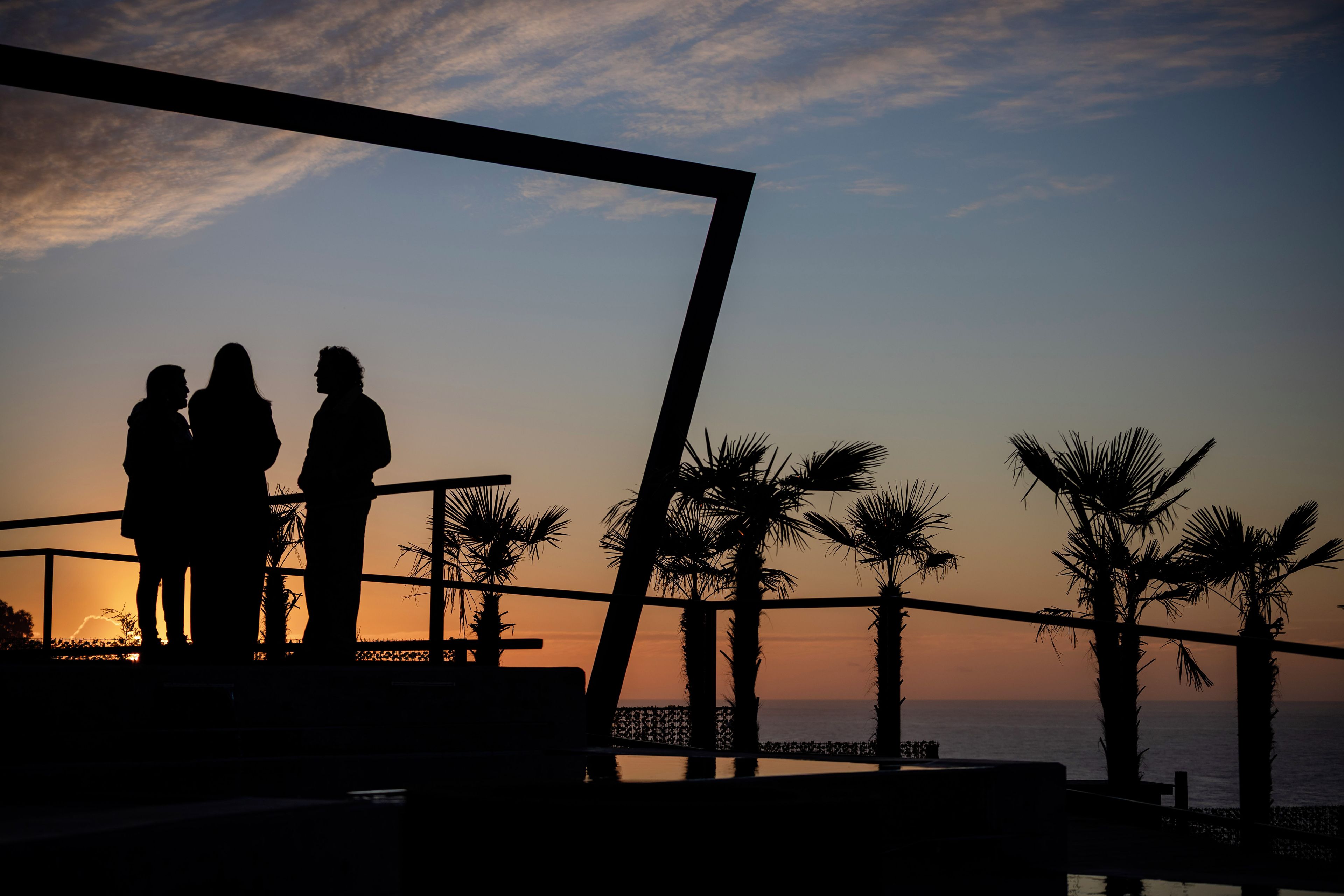 La silhouette de deux personnes se tenant sur un balcon, avec un coucher de soleil en arrière-plan.