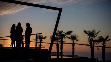 La silhouette de deux personnes se tenant sur un balcon, avec un coucher de soleil en arrière-plan.