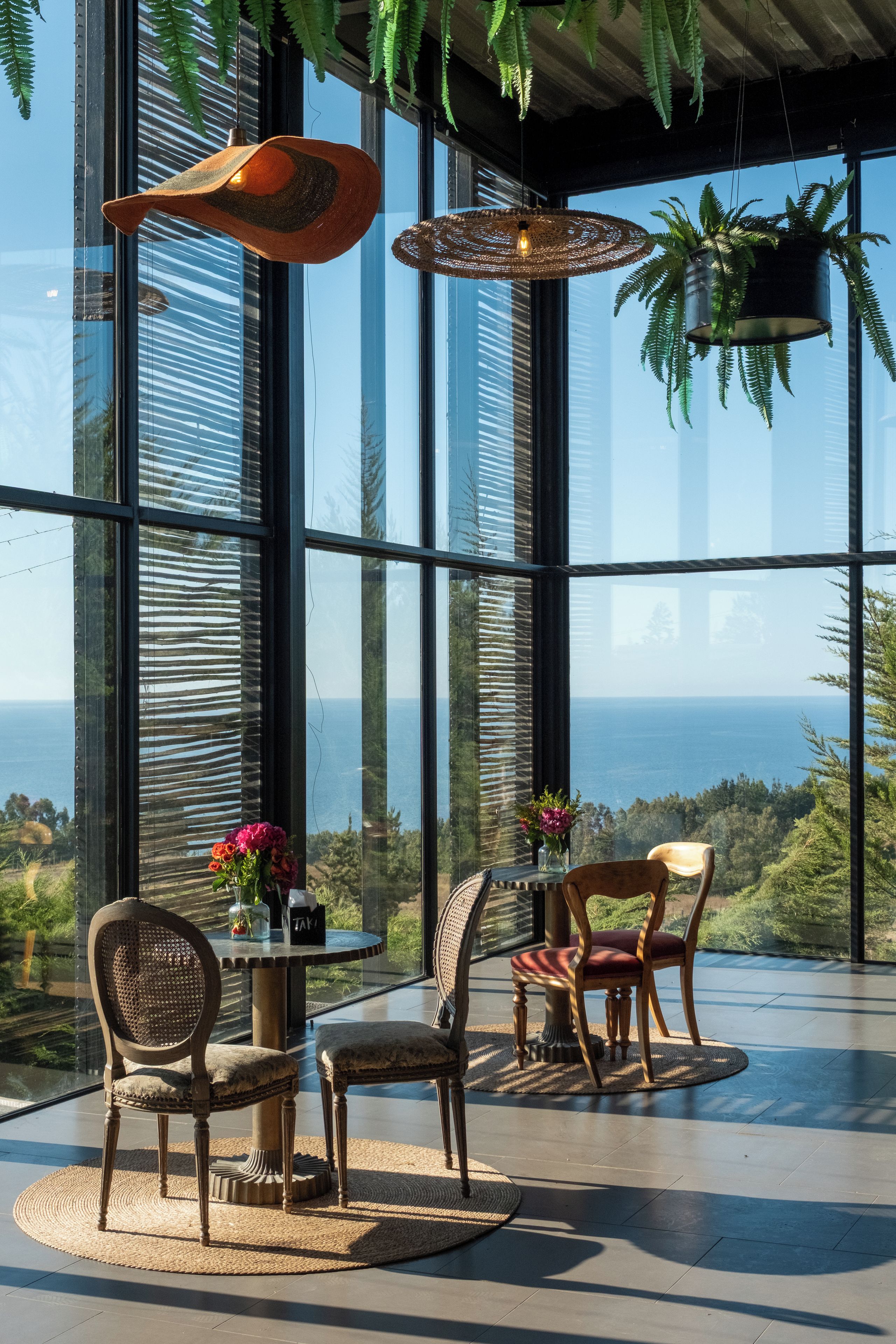 Een modern interieur met grote ramen, een ronde tafel, twee stoelen en hangplanten.