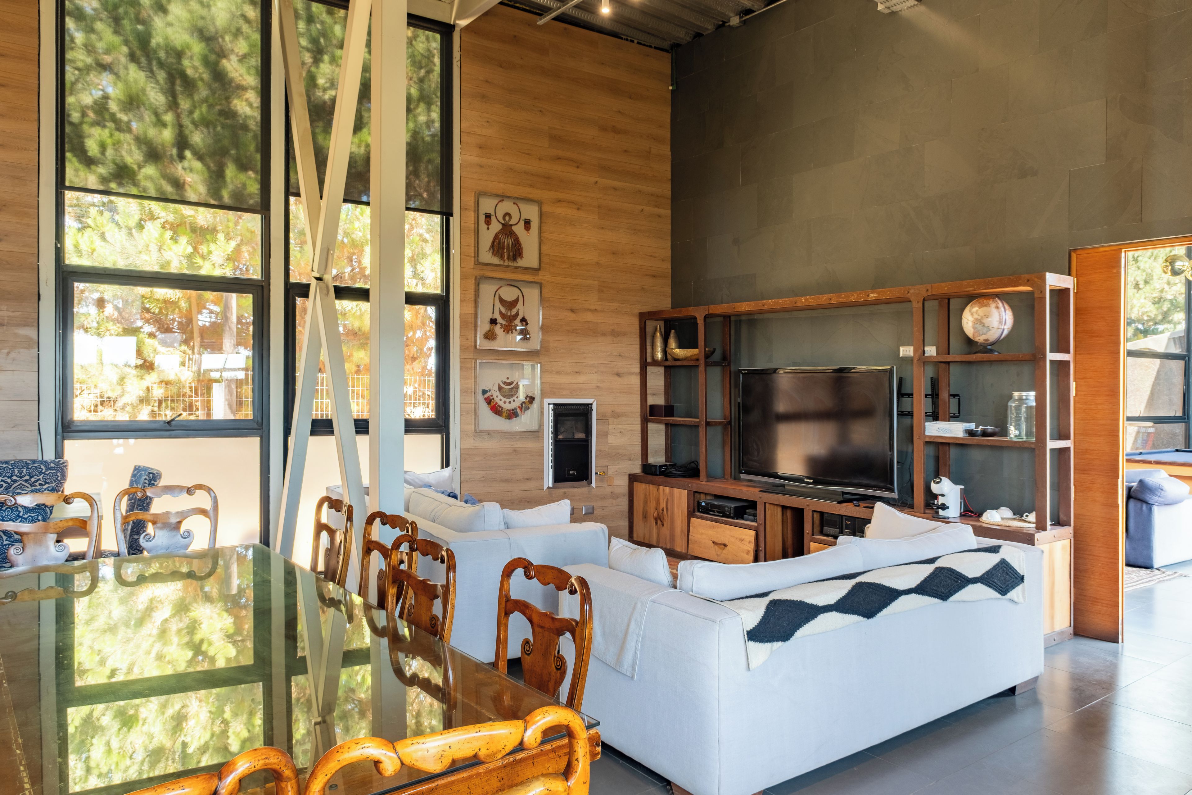 Una sala de estar moderna con una mesa de comedor de vidrio, sillas de madera, un sofá blanco y un televisor de pantalla plana.