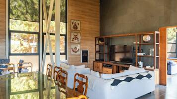 Una sala de estar moderna con una mesa de comedor de vidrio, sillas de madera, un sofá blanco y un televisor de pantalla plana.