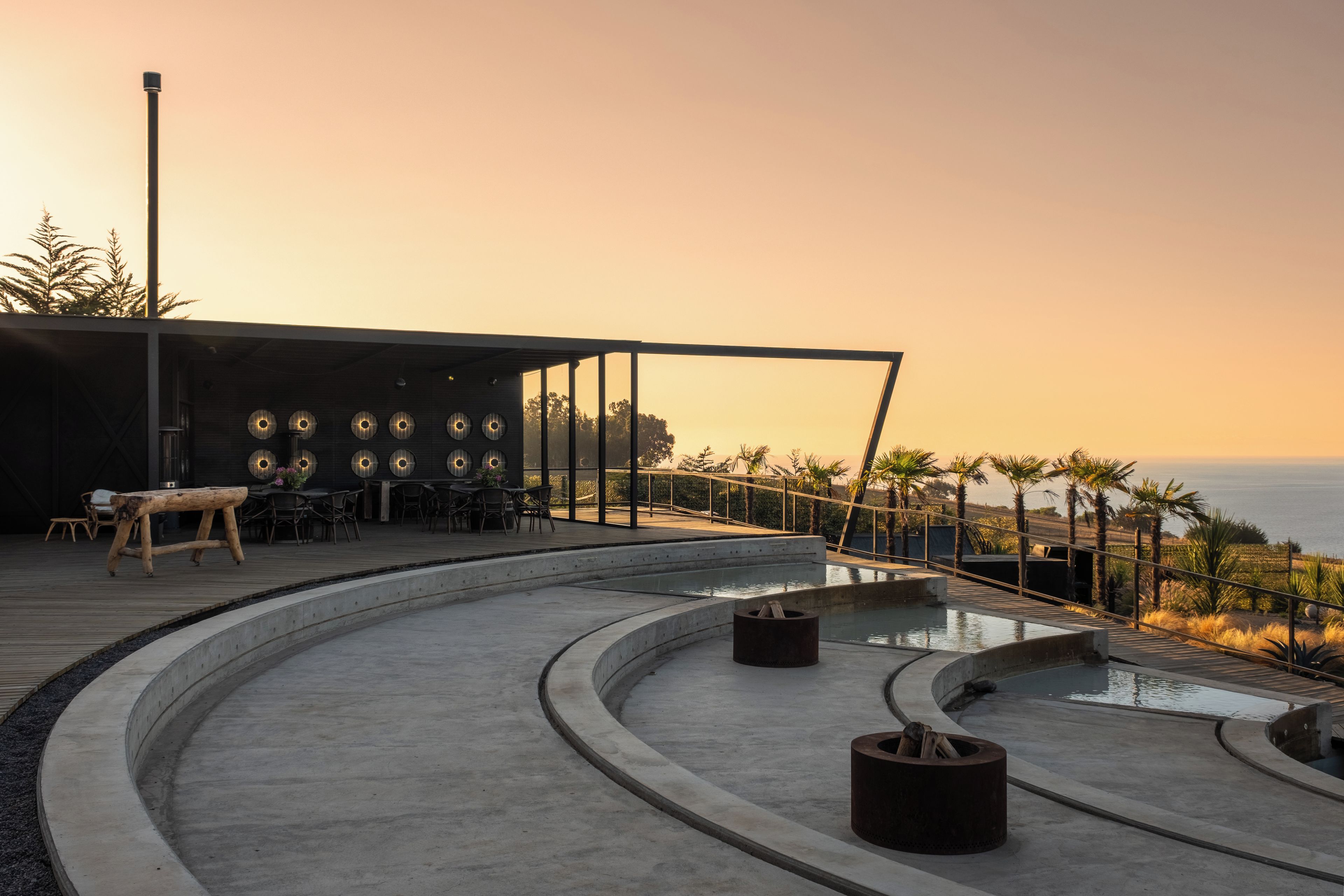 Área de estar moderna ao ar livre com piscina, com vista para a paisagem costeira.