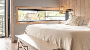 A bedroom with a large bed, a wooden bench, a window with a view, and a woven light fixture. - Taka Matanzas (Navidad)