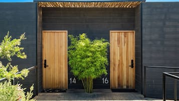A modern building entrance with two wooden doors, numbered 14 and 16, and a bamboo plant in the center.