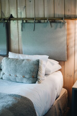 Una cama con sábanas blancas, un cojín de textura gris y un cabecero de madera.