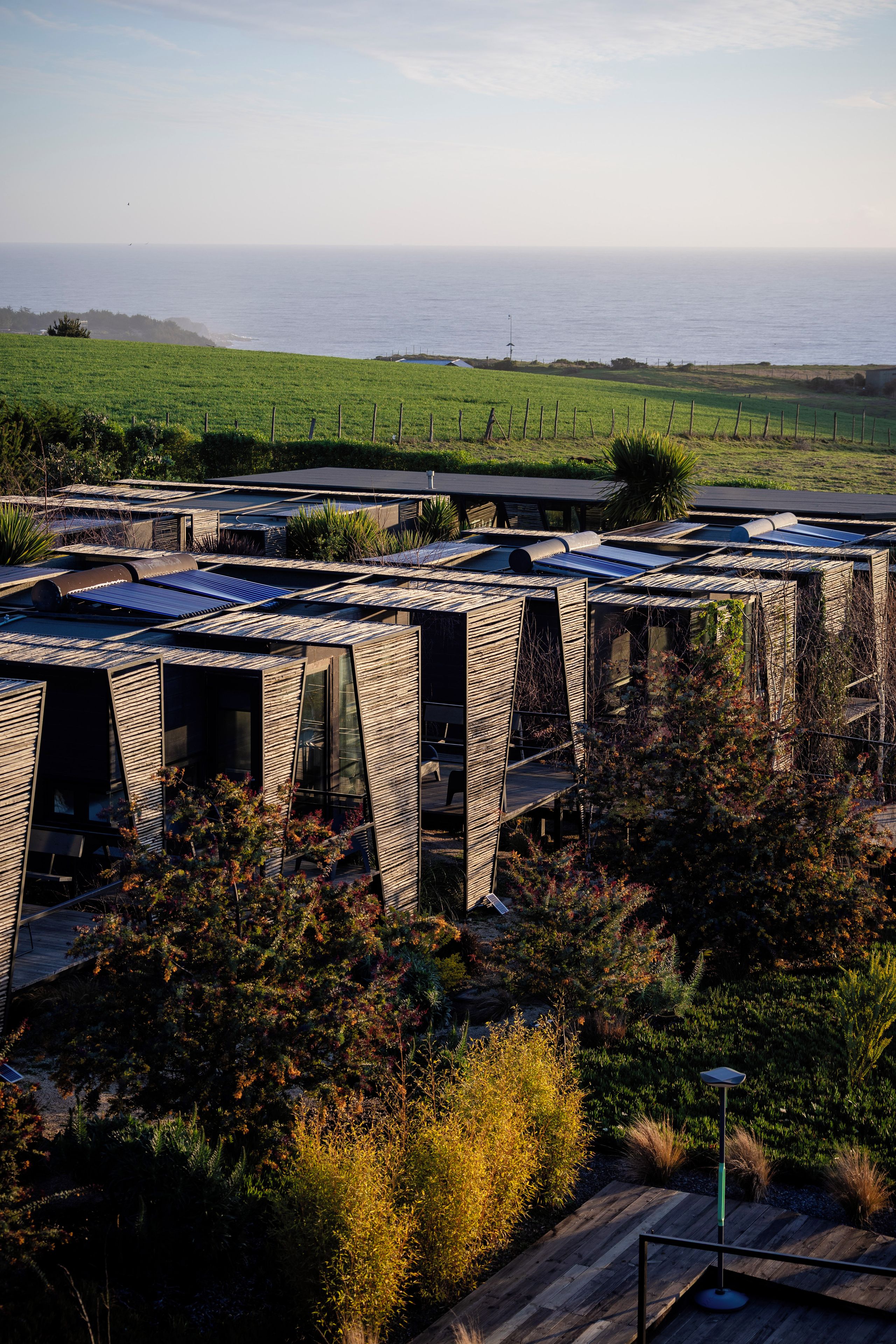 Un edificio moderno con una fachada de madera distintiva, paneles solares y vista al océano.